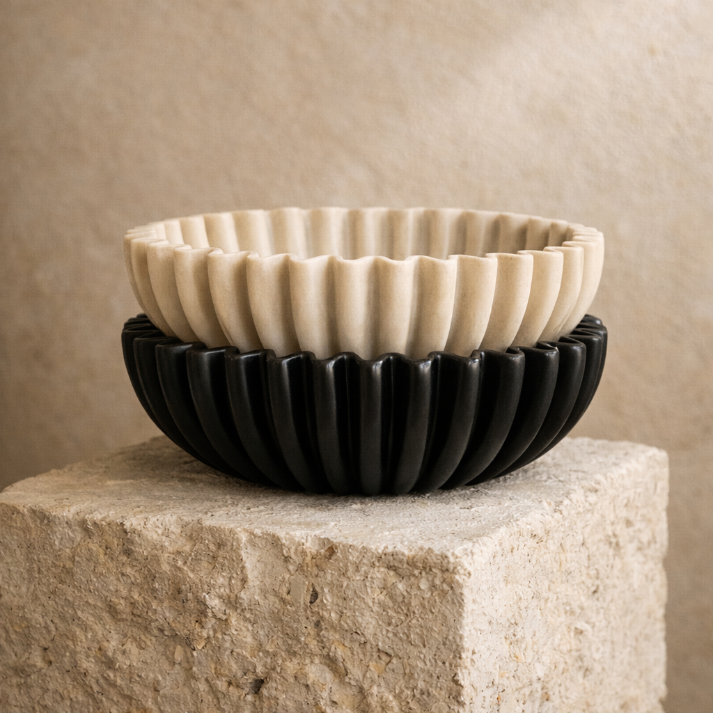 Two ceramic bowls, one black and one beige, stacked on a stone surface with a beige background.