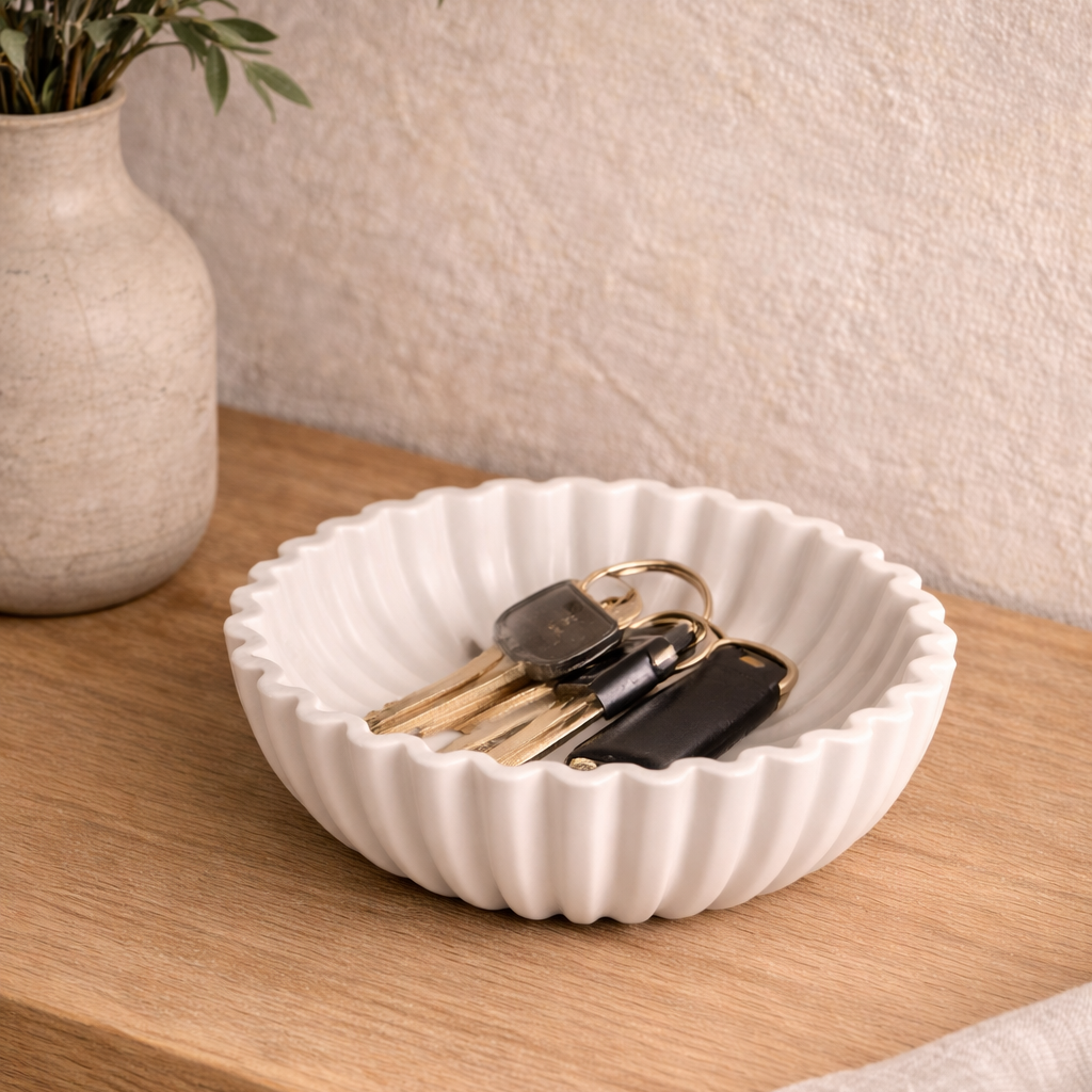White resin bowl with keys on a wooden surface next to a vase.