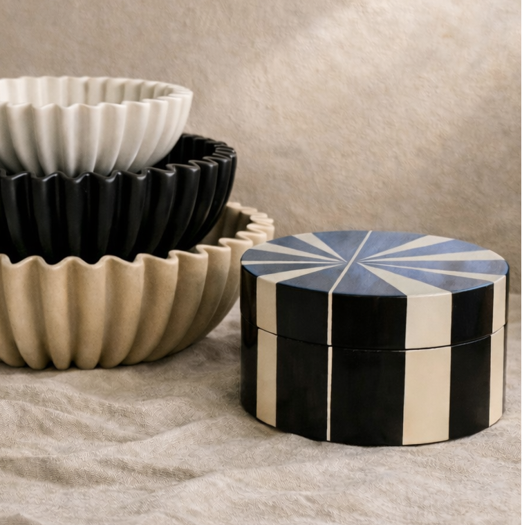A circular decorative box with asymmetrical pattern on a textured surface with a neutral background