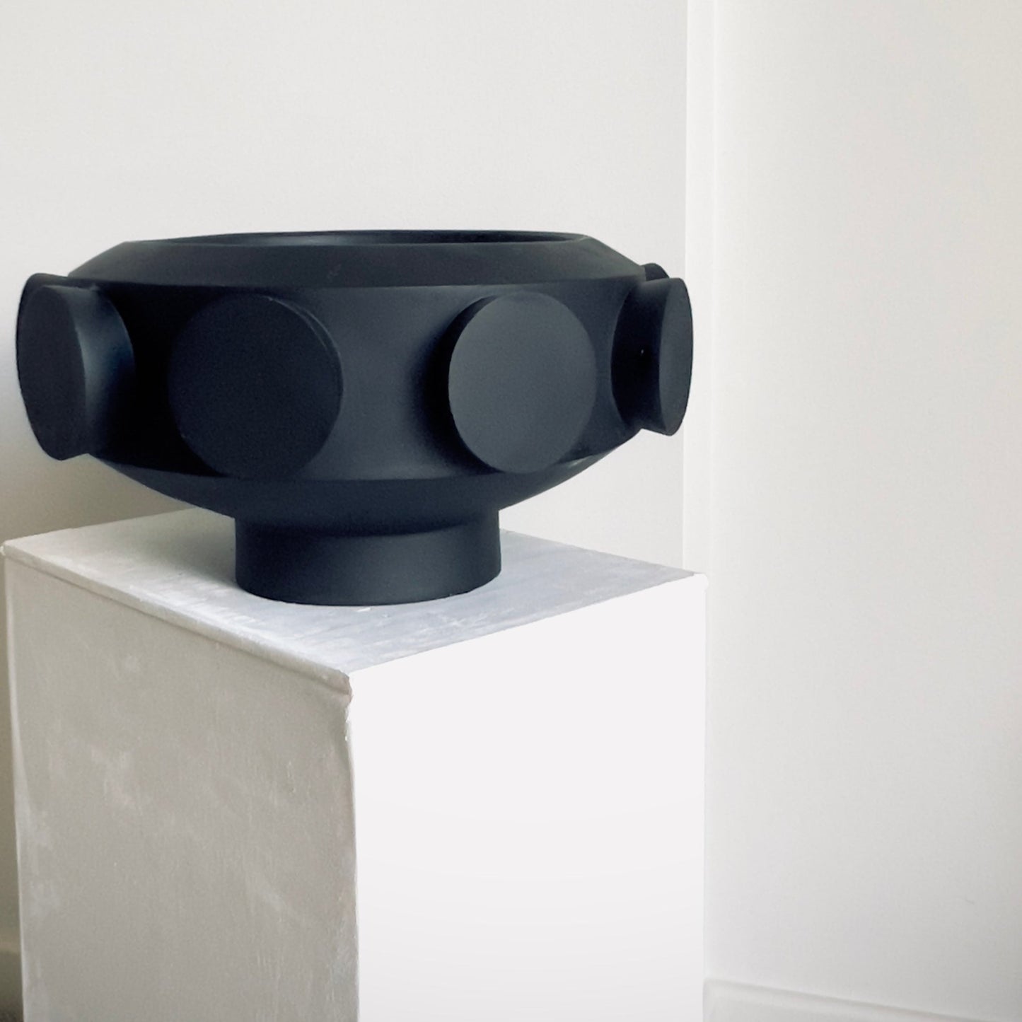 A resin large pedestal bowl with black cylinders on the exterior or perimeter